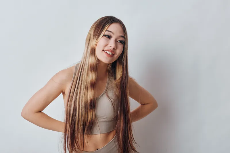 Smiling young woman with long straight hair posing in casual outfit on white background. Happy girl with hands on hips looking aside for lifestyle and beauty portrait.