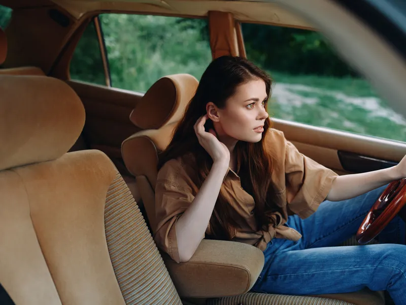 Young woman in casual attire sitting in a vintage car, looking thoughtful, with a relaxed expression and natural background.