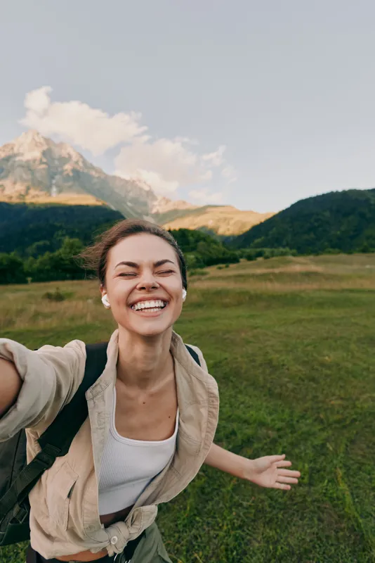 Woman enjoying outdoor lifestyle in a sunny mountain field, smiling during a carefree selfie, embracing nature and adventure in fresh air sun