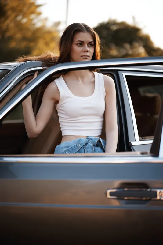 Young woman in casual outfit sitting in a car, looking thoughtfully outdoors, sunlit background, capturing the essence of freedom and adventure.