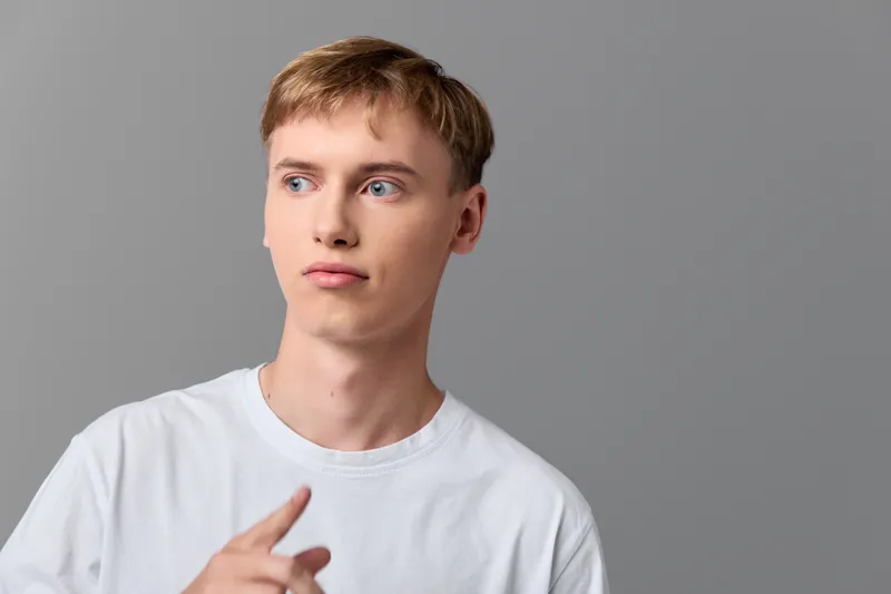 Man, thinking, thoughtful expression with sideways gaze in a casual white shirt, studio shot, minimal backdrop, modern mood, clean lighting, calm posture, subtle everyday vibe