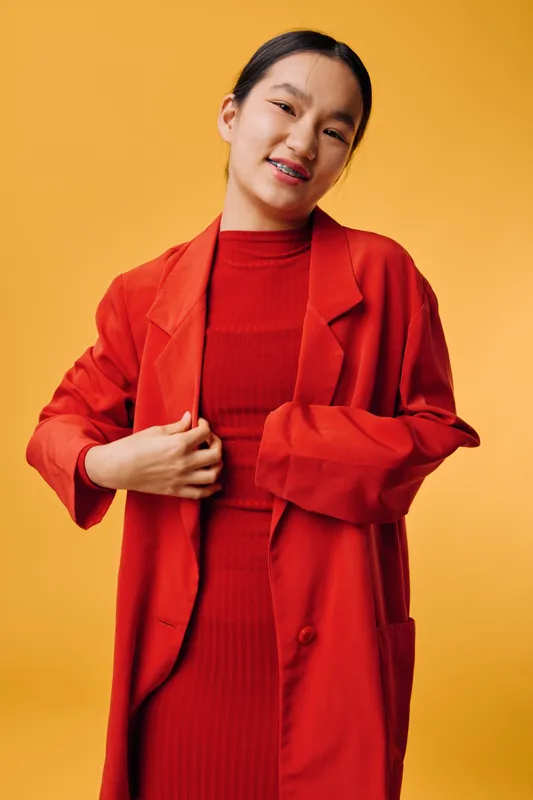 Young woman wearing red coat and dress posing smiling against yellow background studio portrait fashion clothing casual style female model Asian person with braces