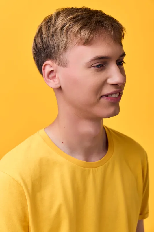 Young man, casual pose, yellow shirt, studio lighting, smiling softly, clean background, fashion vibe, relaxed expression, minimal setup, contemporary style, vibrant tone