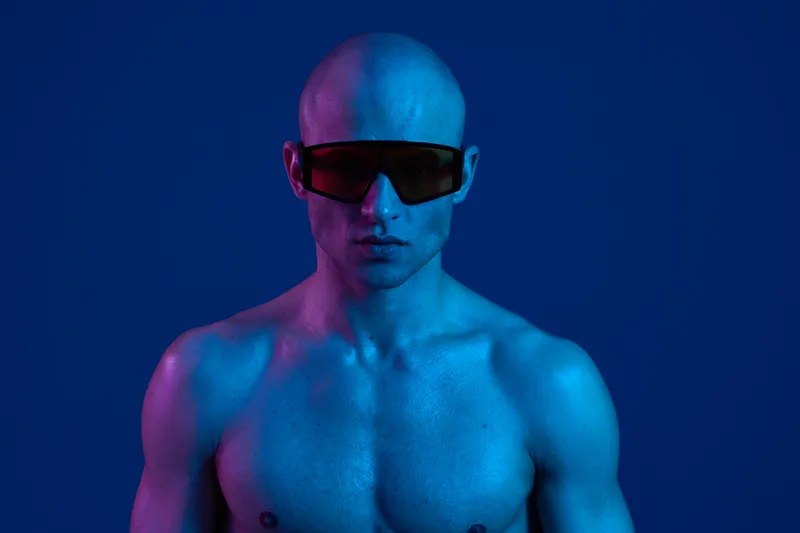 A striking man with a bold look wearing sunglasses, captured in vibrant blue and purple lighting. This image conveys a unique blend of style and attitude.