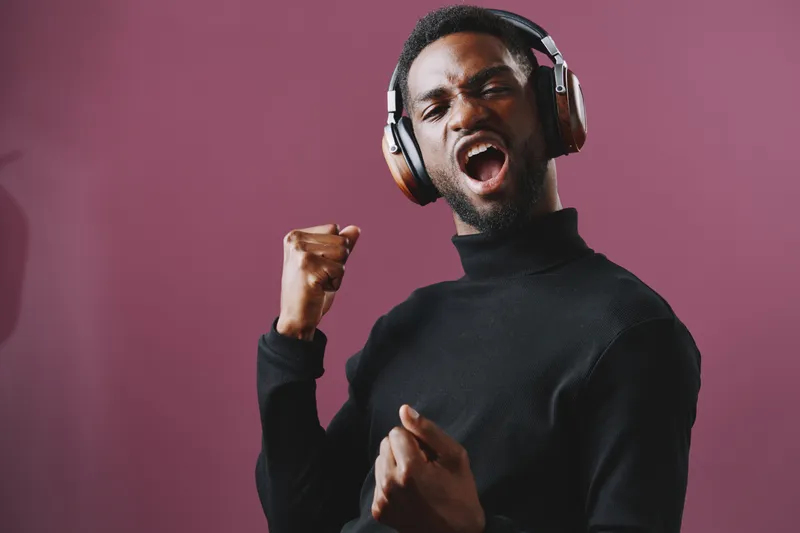 Energetic young man celebrating music with headphones, expressing joy and excitement against a vibrant pink background, perfect for music and lifestyle projects