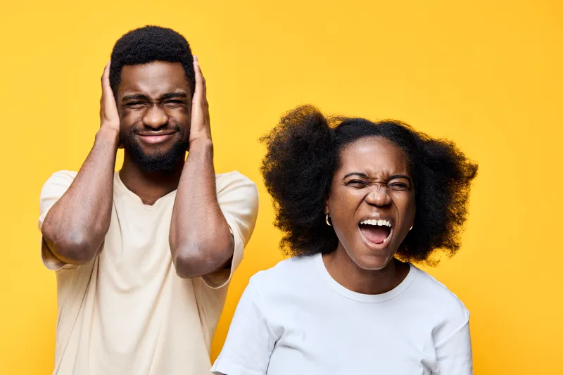 Young African couple expressing joy and excitement against a vibrant yellow background, showcasing emotions of happiness and love in casual attire