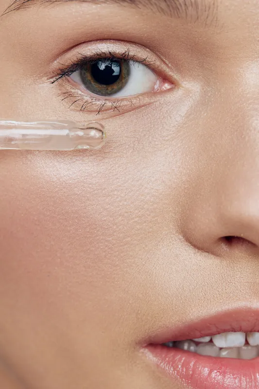 Close up of a young woman applying serum under her eyes, showcasing healthy skin and beauty routine Natural light enhances her fresh appearance and emotion