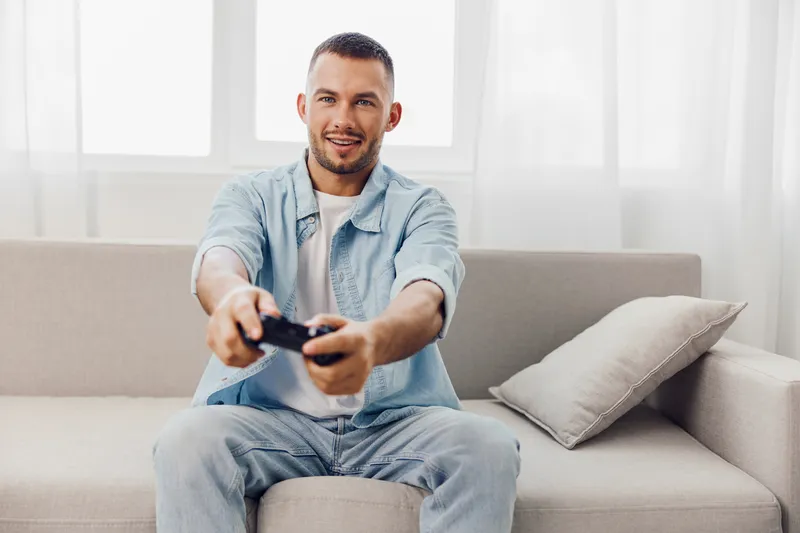 Engaged man enjoying a video game at home, showcasing the joy of leisure, soft masculinity, and emotional wellness in the digital age, embracing authentic imperfection.
