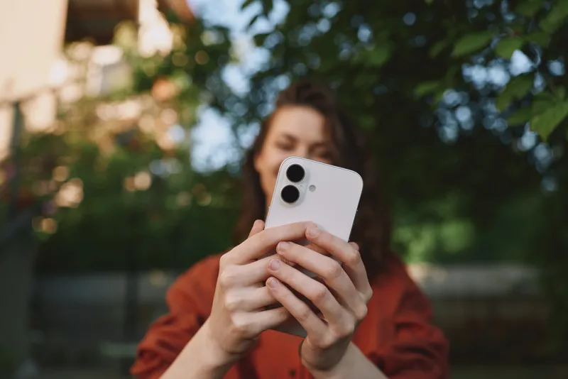 Casual woman outdoors using smartphone, lifestyle portrait with natural daylight, relaxed mood, everyday moment, modern outfit, urban park backdrop, candid vibe, closeup view of device