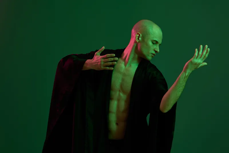 Artistic portrayal of a man in a flowing black robe, showcasing graceful movement against a green backdrop, adding a dynamic and emotional touch to the composition.