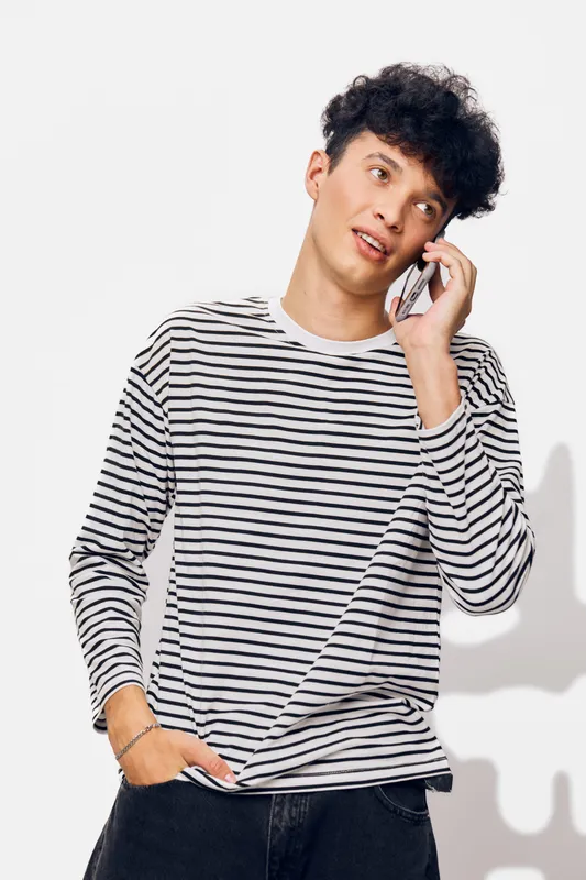 young man talking on smartphone with thoughtful expression wearing striped shirt against plain white background, casual communication concept