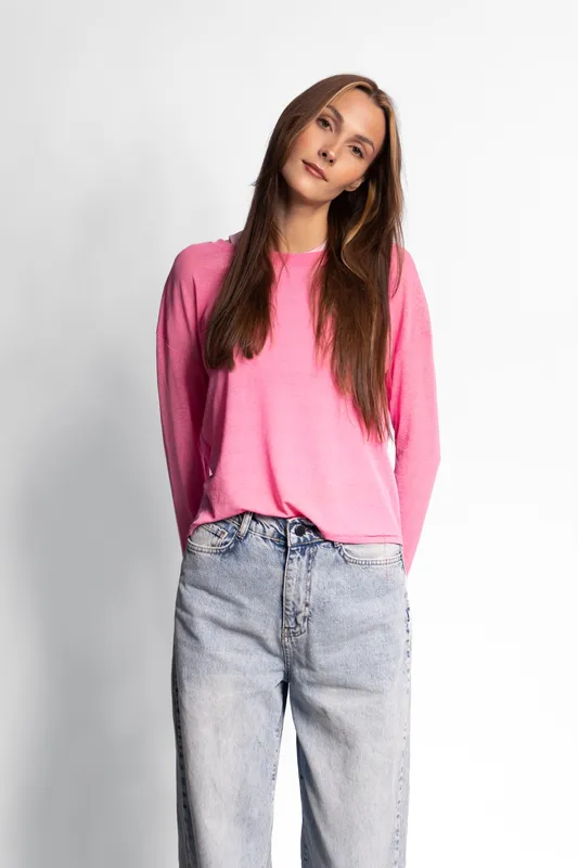 Young woman with long brown hair wears pink sweater and blue jeans standing against white background. Casual style and relaxed pose, concept of fashion and everyday clothing.