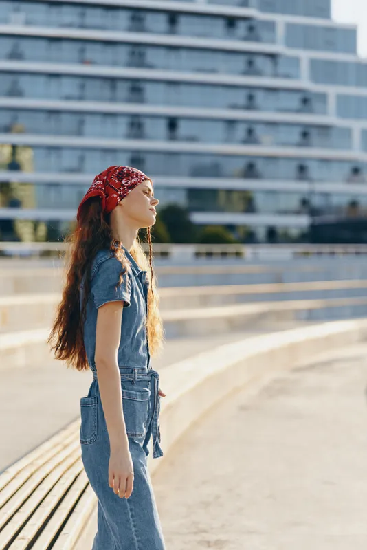 Lifestyle woman in modern boho-western denim street style with film color effect, wearing red bandana and casual outfit outdoors in urban environment.