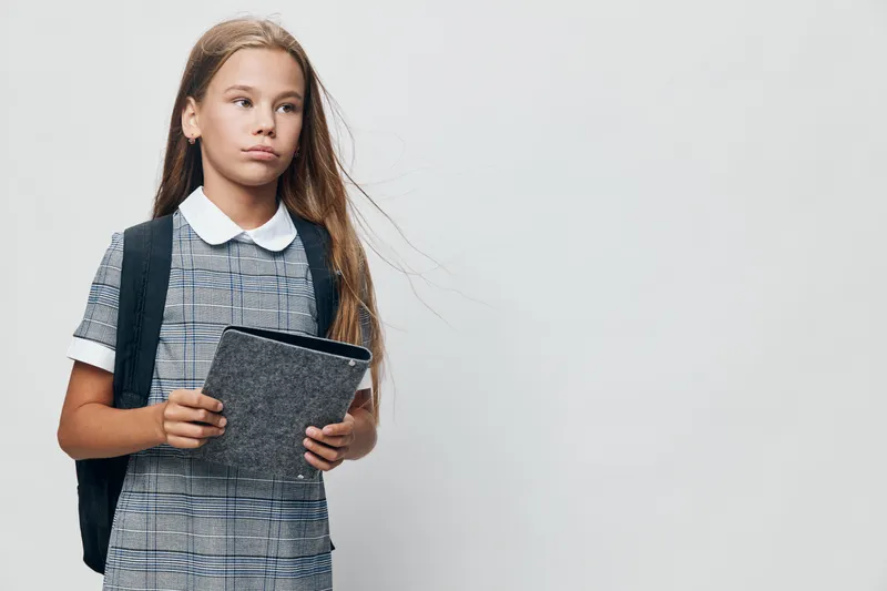 Girl student with backpack holding tablet, standing and looking sideways for education, technology and school learning on white background. Serious child with long hair in uniform.