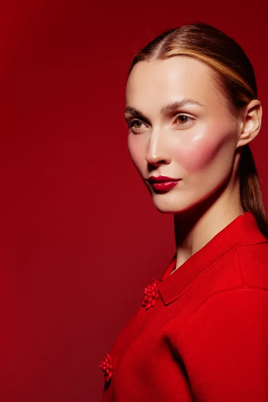 Portrait of a woman with red lipstick and blush wearing a red sweater against a red background. Concept of fashion, beauty, makeup, and elegance in studio lighting.