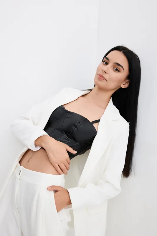 young woman with long black hair wearing white suit and black top posing against a white background, stylish and modern fashion portrait with confident expression