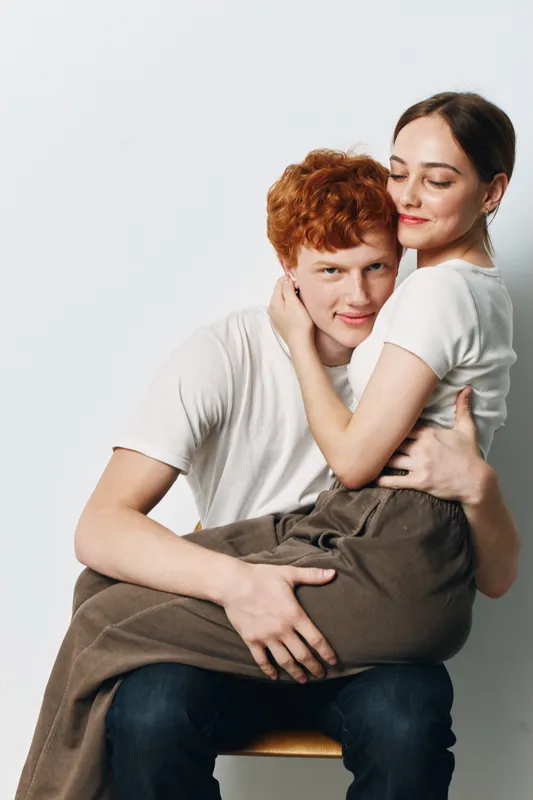 Couple embracing, young man and woman sitting together in casual clothes, showing affection, love and connection on white background portrait.