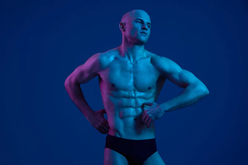 Confident muscular man posing against a vibrant blue background, showcasing strength and determination. The image captures a powerful expression and dynamic lighting.