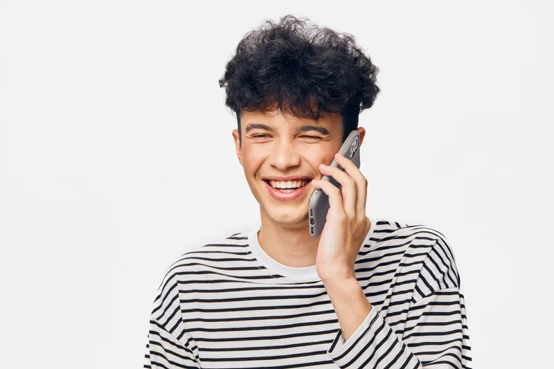 smiling man talking on phone wearing striped shirt expressing joy and friendliness, casual communication, isolated white background portrait