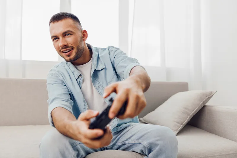Engaged man playing video games at home, showing the balance between relaxation and technology use. A moment of joy and connection in a digital world.