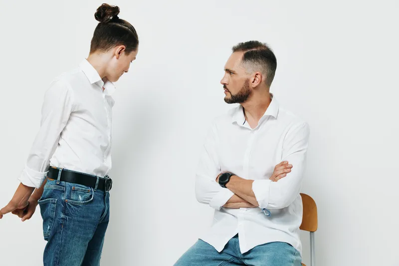 A composed business professional man stands with folded arms, engaging a colleague with a calm, focused expression against an isolated colored background.