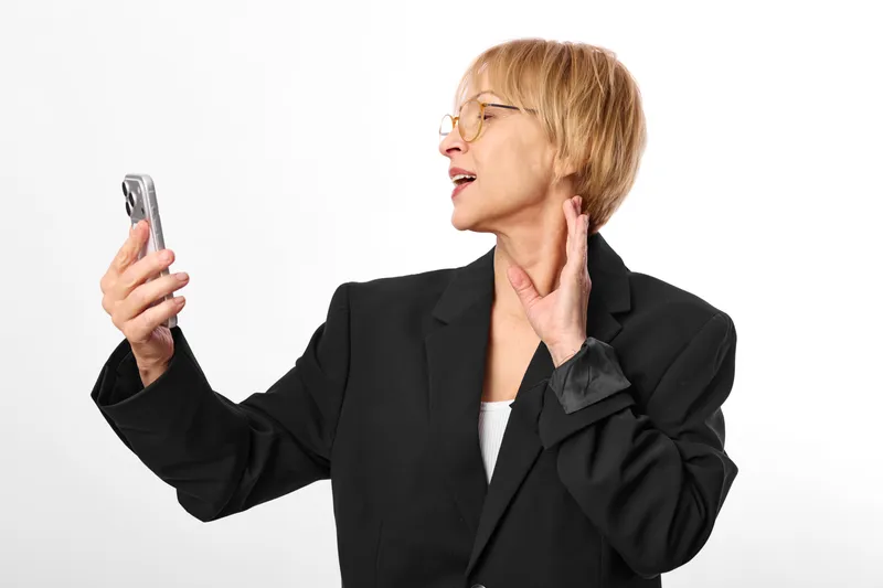 Stressed business woman in black suit holds smartphone and touches cheek, looking anxious and overwhelmed. Concept for stress, burnout, and mental health at work.