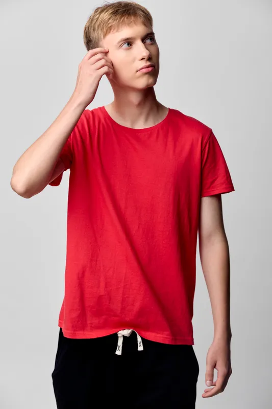 Man in a red t shirt thinking, casual style, studio shot with plain background, relaxed pose, modern streetwear vibe, simple wardrobe, thoughtful expression, fashion stock image for lifestyle