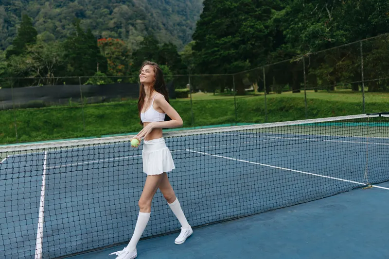 Young athletic woman playing tennis on a sunny court, wearing a white outfit, exuding confidence and joy in a lush green environment