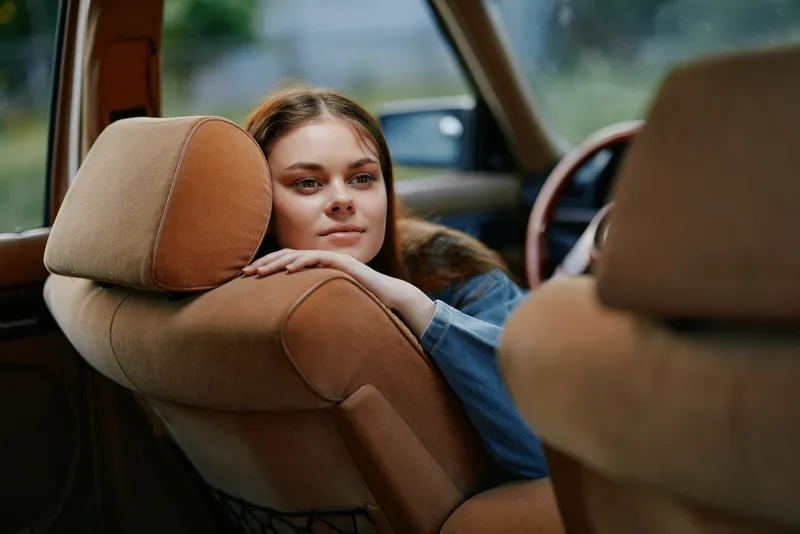 Young woman relaxing in a vintage car, showcasing a serene expression and natural beauty, perfect for lifestyle and travel themes.