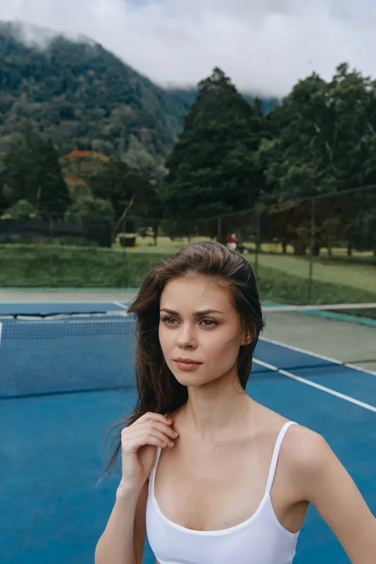 Young woman in sportswear on a tennis court with a scenic mountain background, embodying fitness and healthy living in an active lifestyle