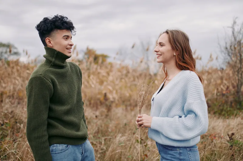 Two young adults stand in a windswept field, sharing a warm, candid conversation that highlights authentic human connection and everyday moments grounded in honesty and reliability. (169 characters)
