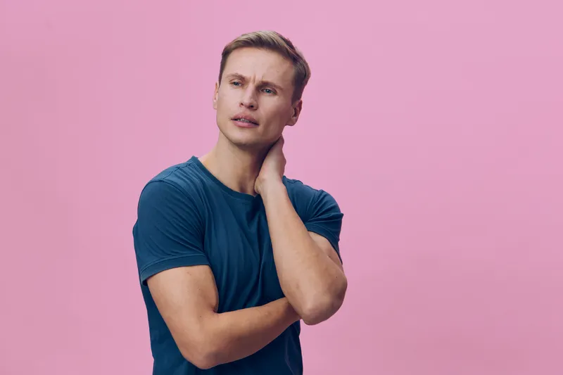 Young thoughtful man in blue t-shirt looking away touch neck isolated on pink background health mental wellbeing concept portrait
