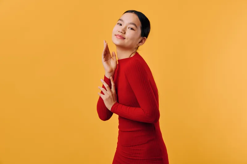 Woman in red dress posing with confident smile against yellow background, fashion portrait with elegant makeup and stylish earrings for beauty and style concept.