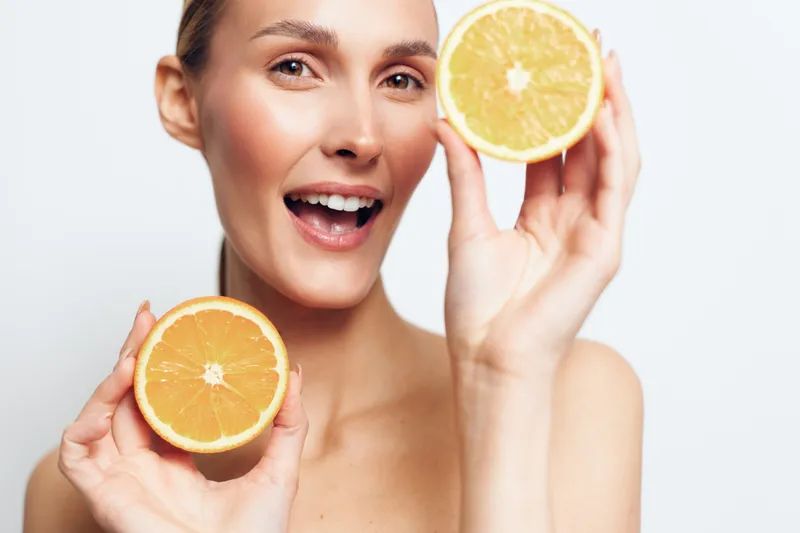 A cheerful woman holds halved oranges, showcasing bright citrus and a fresh, healthy vibe. Close-up portrait with vibrant color, summery mood and upbeat wellness.