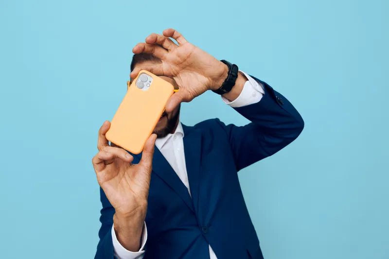 Professional business man on a solid blue background, self portrait with a mobile phone, conveys confidence, curiosity, and energetic focus in a modern work vibe.