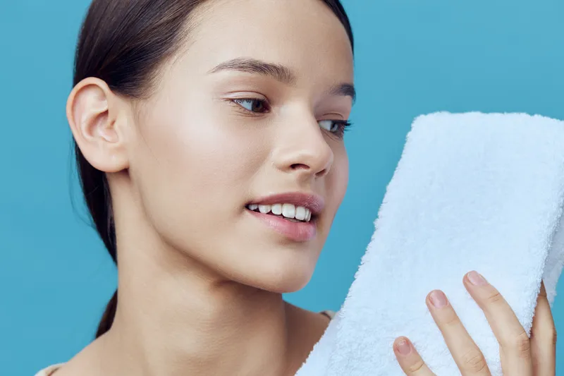 Young woman with a towel, showcasing a clear complexion and natural beauty against a serene blue background, representing skincare and self care routines