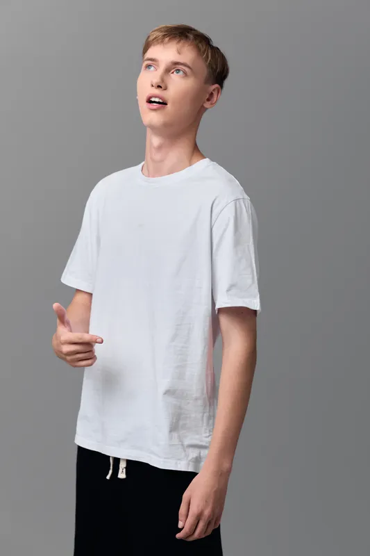 Young man, white t shirt, casual fashion, looking up, studio shot, relaxed pose, everyday wear, fashion photography, minimal backdrop, clean look, expressive gaze, candid style