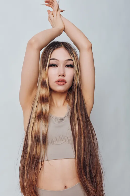 Young woman with long straight hair posing with arms raised above head against gray background. Beauty, fashion, hairstyle and confident female model with natural makeup and modern style.