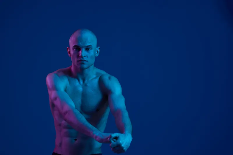 Athletic man posing with confidence under blue lighting, showcasing strength and determination in a dramatic, low-light environment. Perfect for fitness themes.