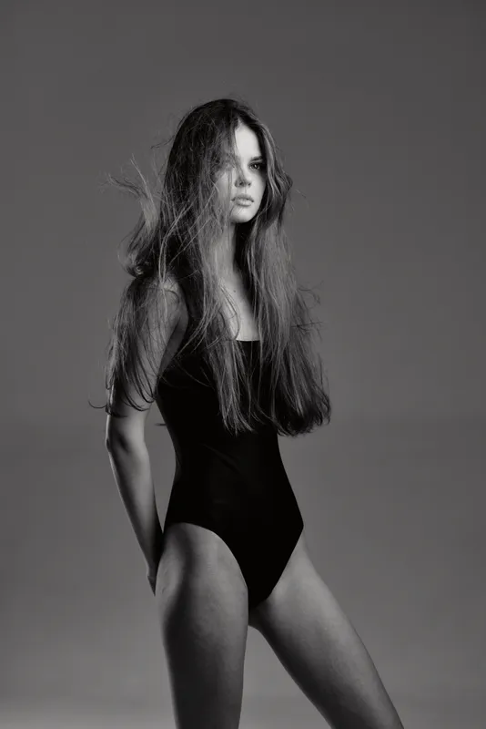 Black and white portrait of a slim woman in a black bodysuit with long hair in a studio setting