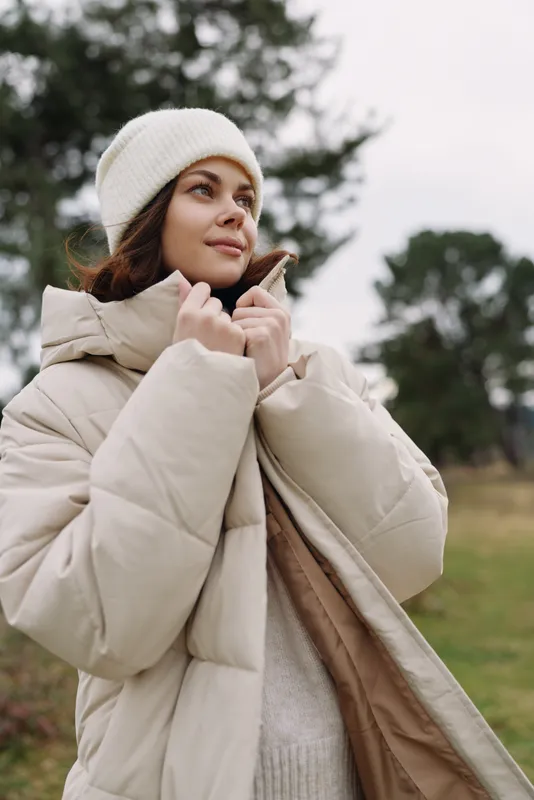 Woman in a warm coat outdoors during winter, wearing a beanie and puffer jacket, enjoying the chilly day with a calm, stylish look and cozy comfort