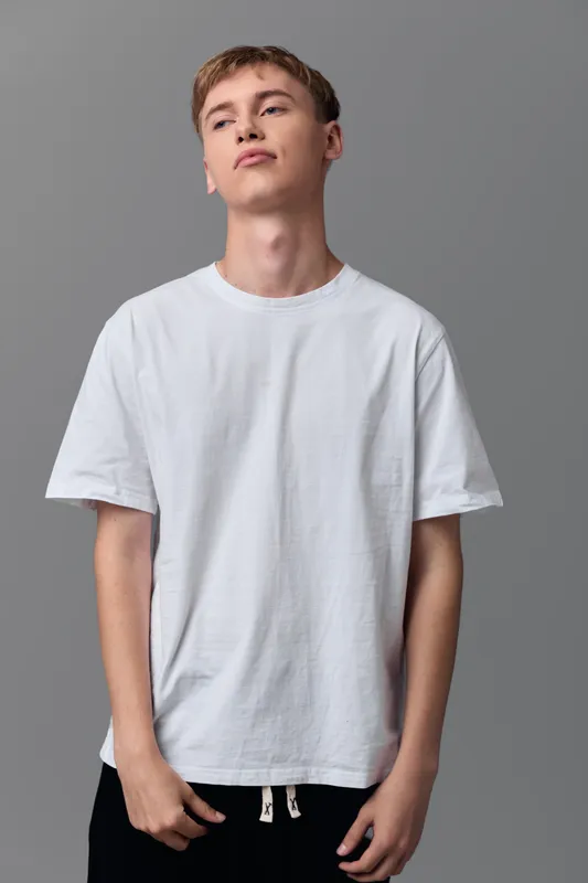 White t shirt worn by a young man in a casual, minimalist studio shot highlighting basic apparel and a relaxed stance against a neutral gray backdrop