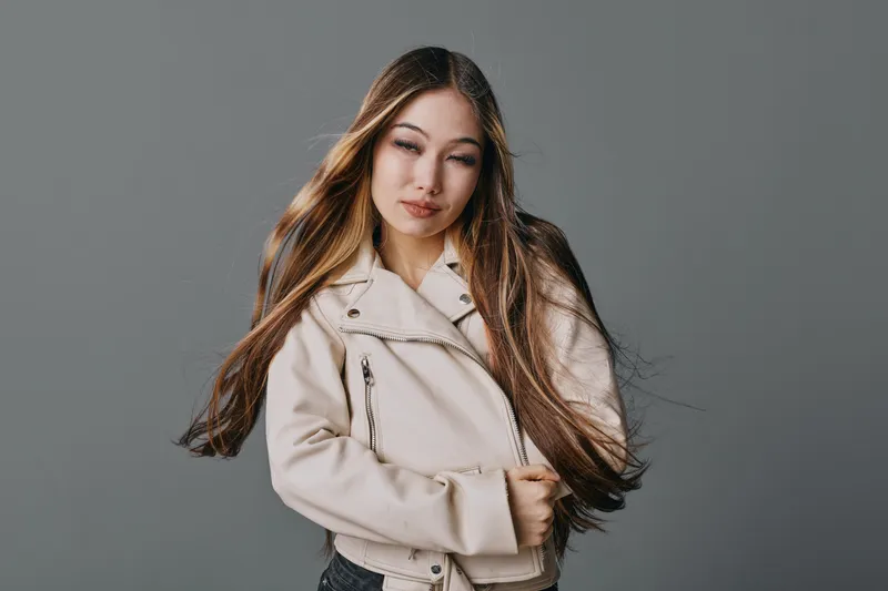 Young woman with long hair wearing beige jacket and posing on gray background confident look in studio. Fashion portrait with natural makeup and casual style for lifestyle or beauty.