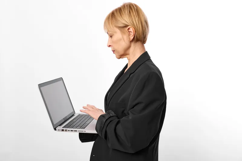 Woman typing on laptop, office work, side view against white background, focused expression, professional business attire, computer setup, clean minimal scene