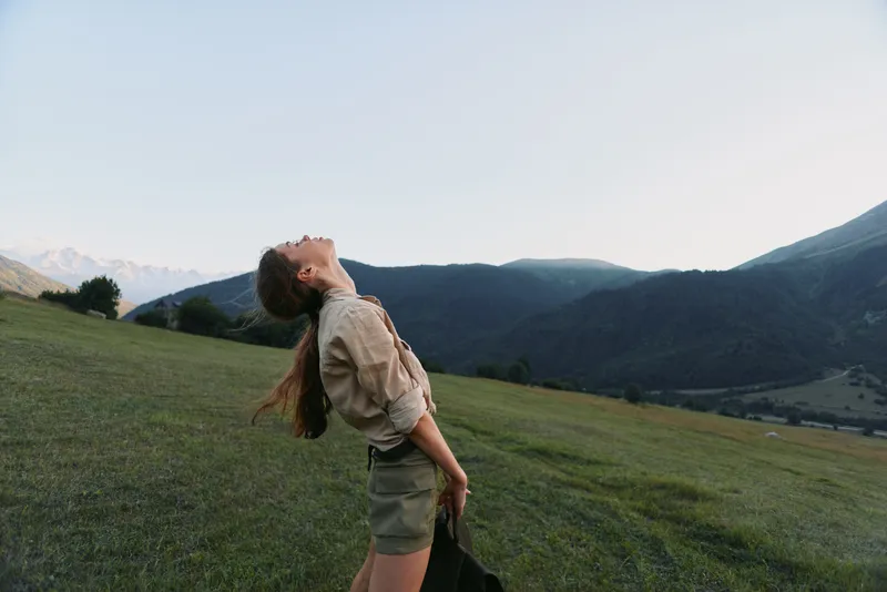 Cheerful woman lifestyle outdoor countryside portrait casual, nature, sunshine, mountains and meadow, relaxed pose, sunlit breeze, blue sky, authentic candid moment in nature