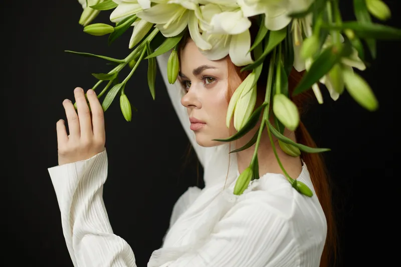 Elegant young woman with long red hair adorned with a floral crown of white lilies, showcasing beauty and artistry in a minimalist portrait