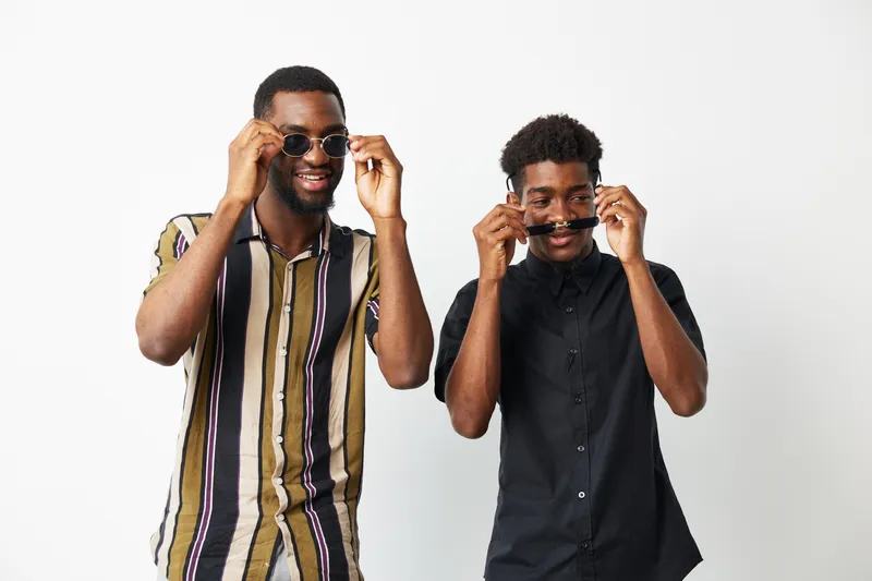 Two smiling African American men wearing stylish sunglasses, showcasing confidence and friendship against a minimalistic backdrop. Perfect for fashion and lifestyle themes.