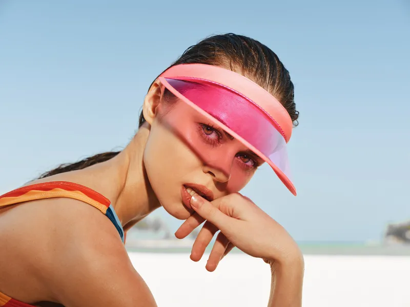 Close-up of a sunlit beach model wearing a pink visor and colorful swimwear, with a relaxed pose and confident gaze, capturing summer fashion and outdoor leisure.