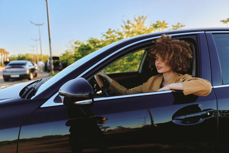 Woman lifestyle driving car outdoors, sunny casual relaxed smile, driver in a car enjoying a moment of daily travel, warm light, candid atmosphere, peaceful moment