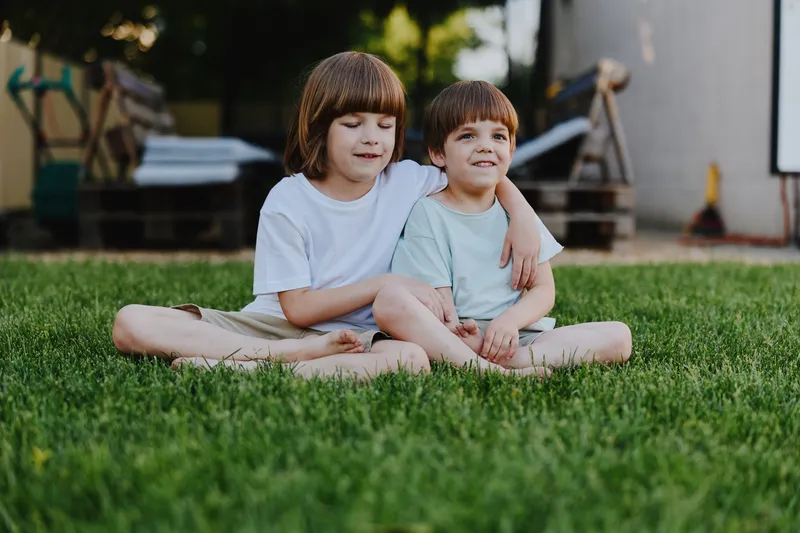 Happy children sitting together on green grass, enjoying a sunny day outdoors, creating a joyful moment full of love and friendship.